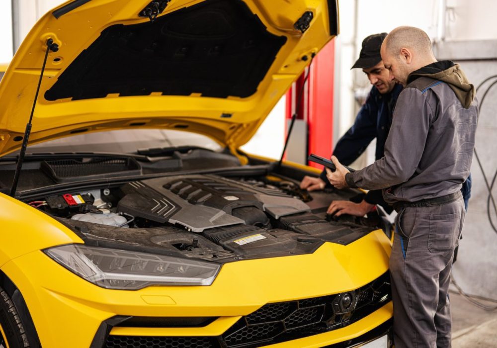 two-mechanics-stand-with-tbalet-against-open-hood-of-yellow-sport-car-suv-.jpg